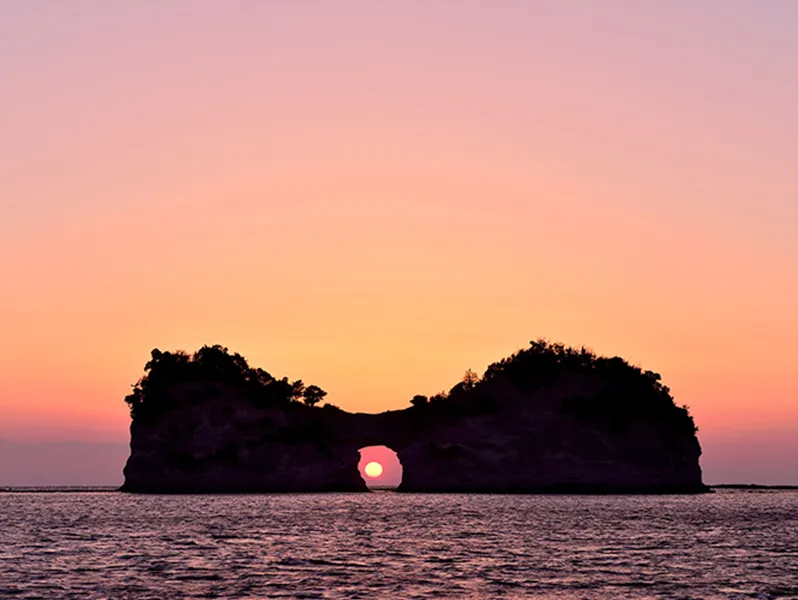 夕日が沈む海と、島に空いた穴から見える太陽。