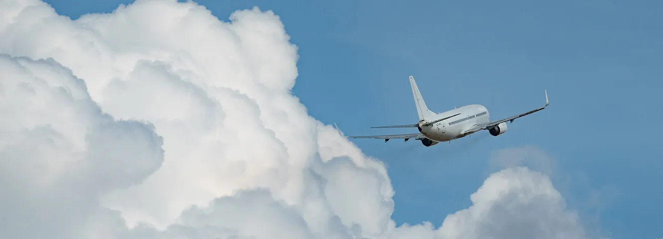 青空に浮かぶ白い雲と、上昇する飛行機。